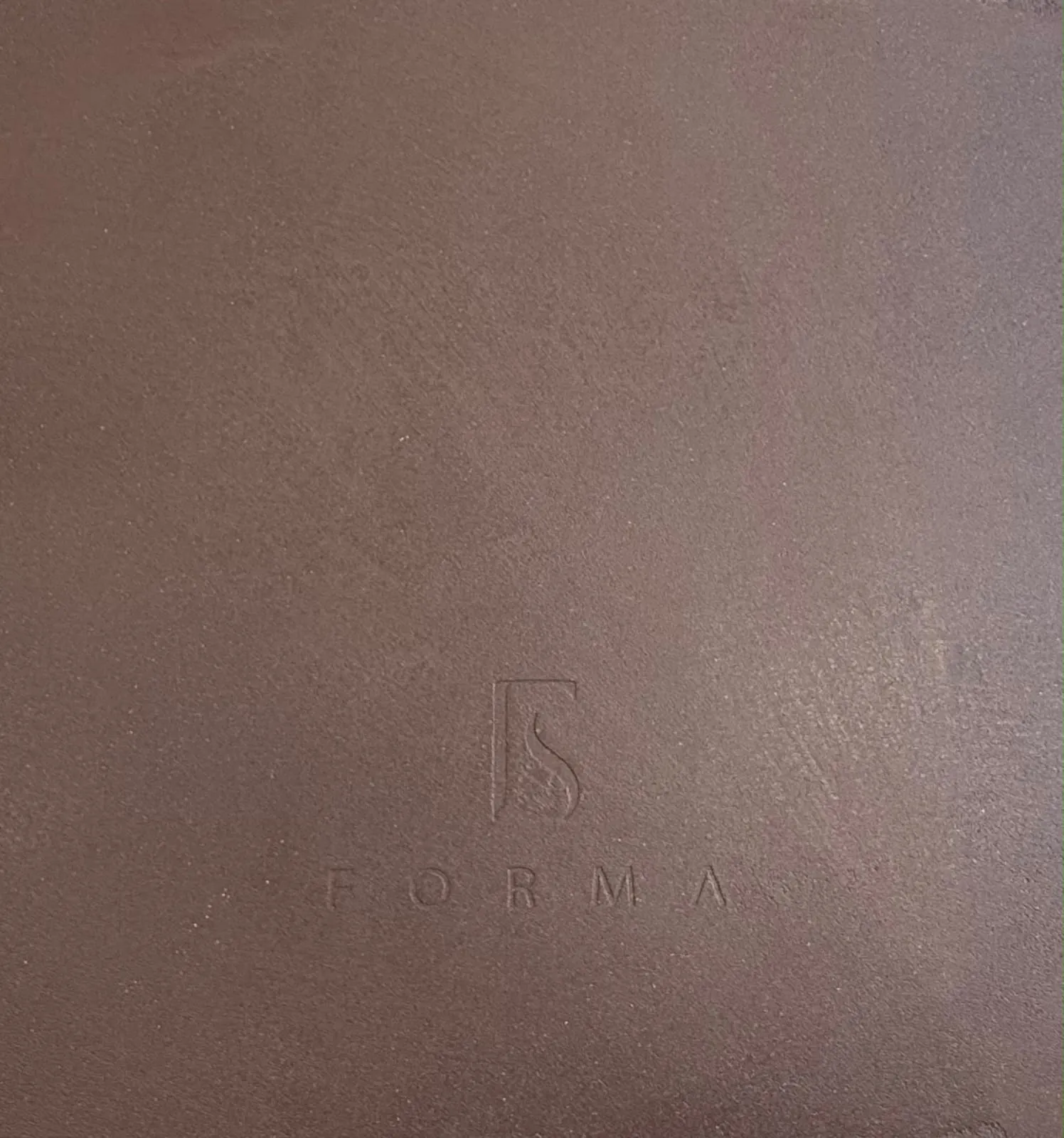 Terracotta Oltre microcement sample with the Forma mark pressed into the surface