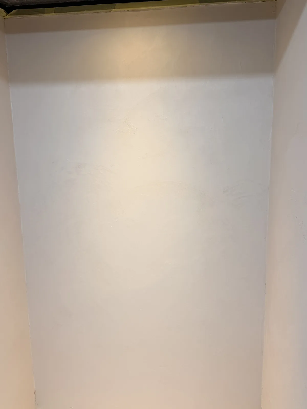Smooth white Oltre microcement finish in a recessed wall niche under a spotlight